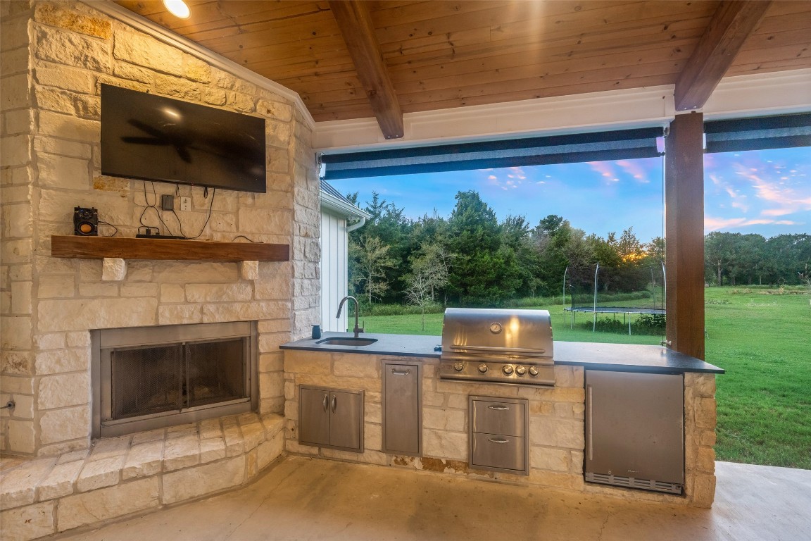 27201 Double Culvert Road Hempstead, TX 77445 - Photo 10 of 49 Stone-accented outdoor kitchen with built-in grill, sink, and refrigerator, all under the warmth of a wood-paneled ceiling.