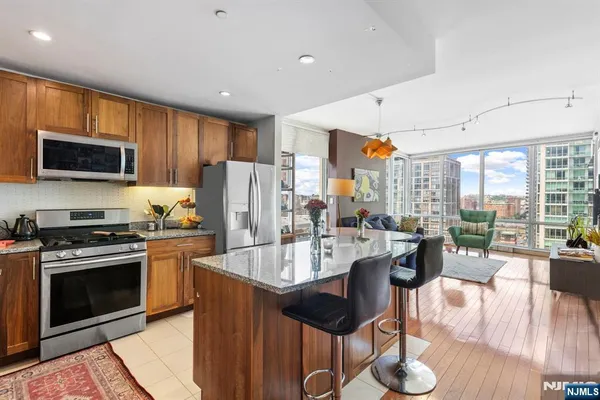 a kitchen with stainless steel appliances granite countertop a refrigerator a stove top oven a sink dishwasher and couches with wooden floor