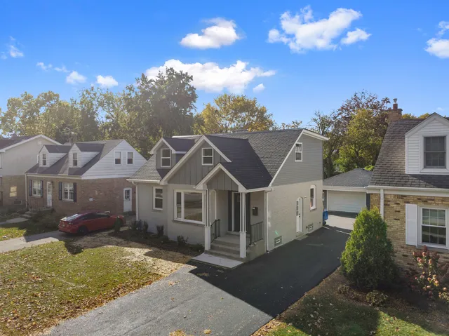 a view of a white house next to a yard with plants and large trees