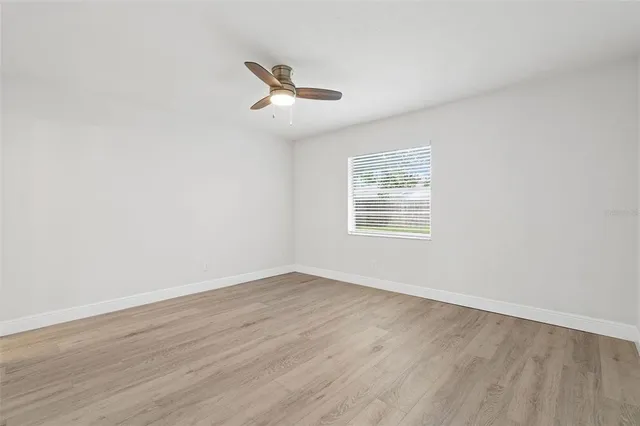 an empty room with wooden floor fan and windows