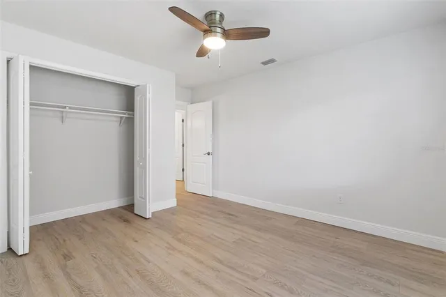 an empty room with wooden floor ceiling fan and window