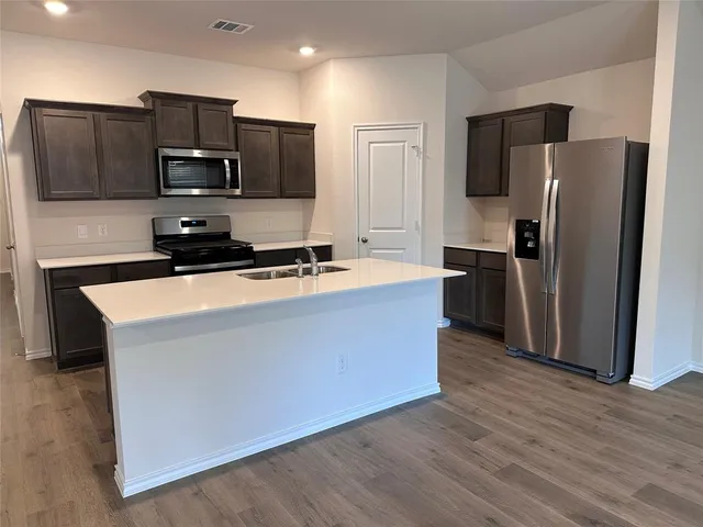 a kitchen with stainless steel appliances a refrigerator a stove a sink a microwave and wooden floor