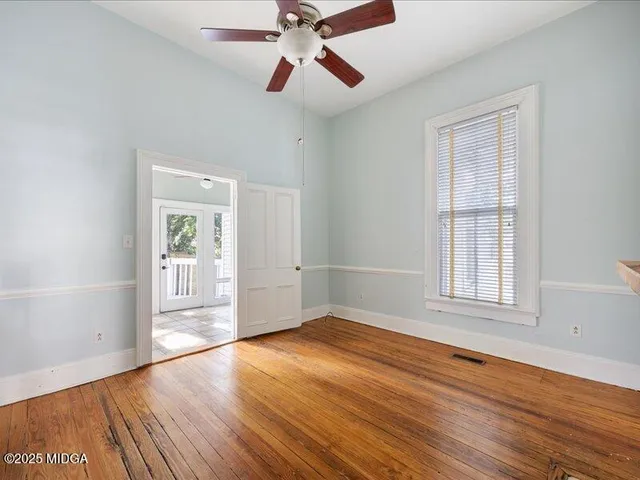 an empty room with wooden floor chandelier fan and windows
