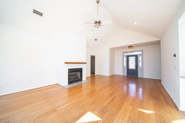 a view of an empty room with wooden floor fireplace and a window