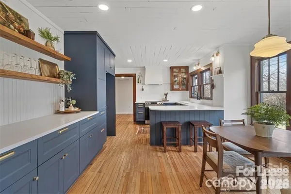 a dining hall with stainless steel appliances kitchen island granite countertop a dining table chairs and a wooden floor