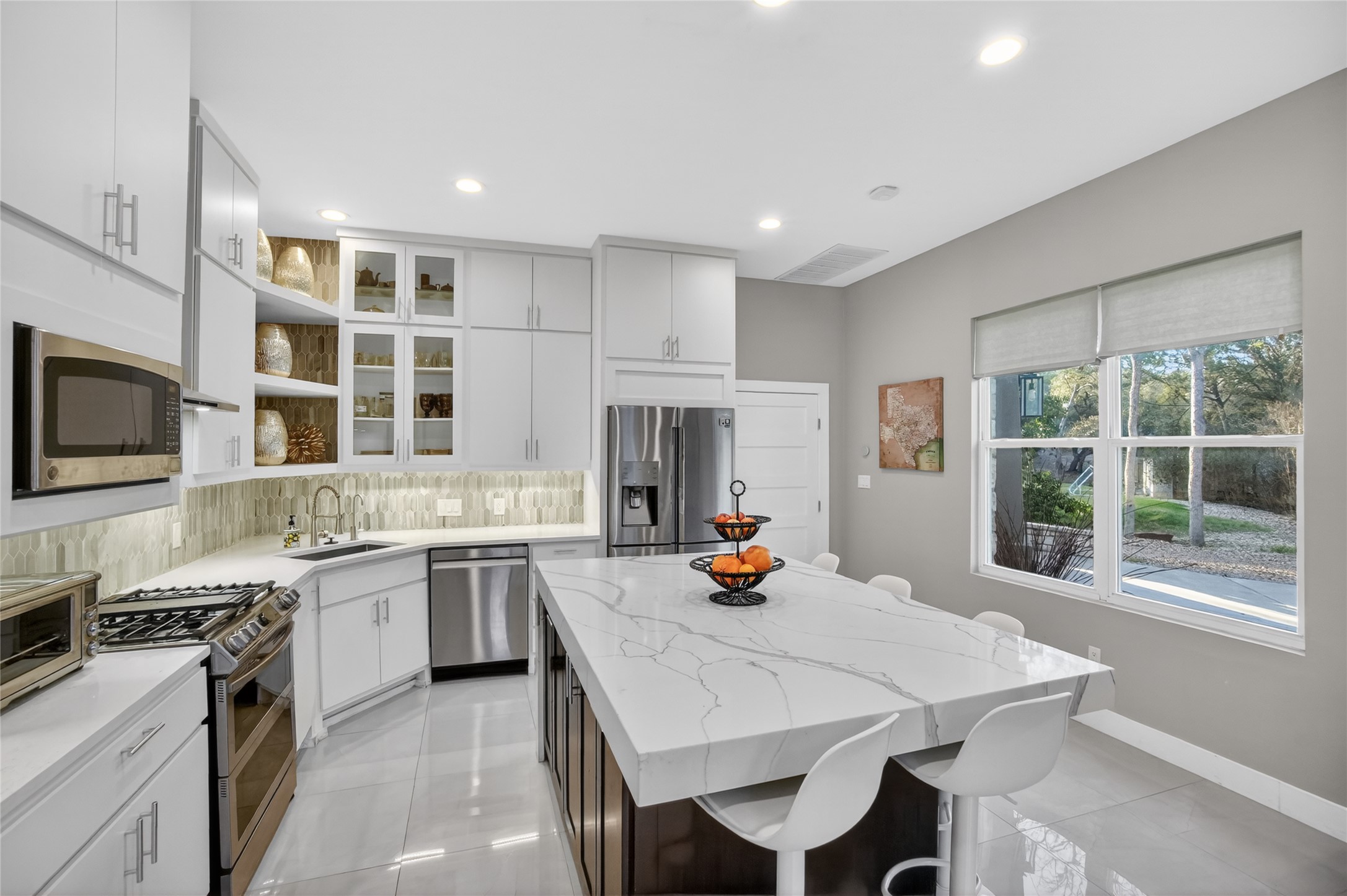 3627 Stoneridge Road Austin, TX 78746 - Photo 27 of 40 Dual tone kitchen with a breakfast bar, glass insert cabinets, a kitchen island, stainless steel appliances, and open shelves