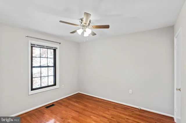 an empty room with wooden floor fan and windows