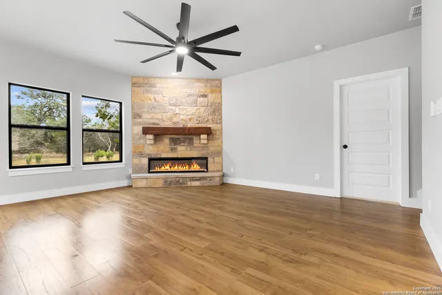 an empty room with wooden floor chandelier ceiling fan and windows