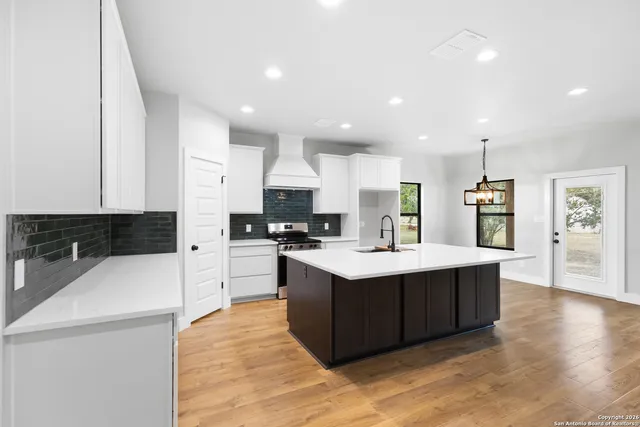 a large kitchen with kitchen island a sink a stove a refrigerator and white cabinets with wooden floor