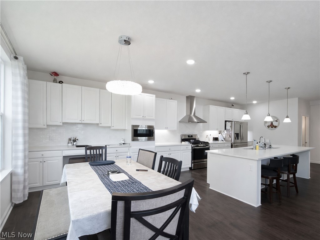 4509 Millbrook Way Akron, OH 44321 - Photo 7 of 27 Open-concept kitchen and dining area featuring dark wood-finish flooring, white cabinetry, integrated stainless steel appliances, a center island with pendant lighting, and recessed ceiling lights