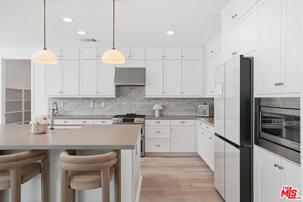 a large kitchen with stainless steel appliances kitchen island granite countertop a dining table chairs and white cabinets