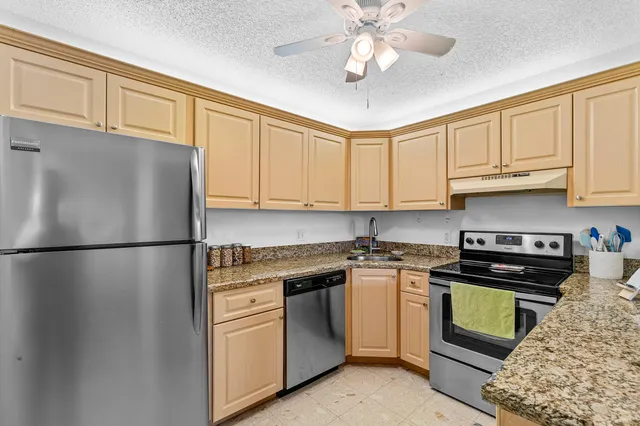 a kitchen with stainless steel appliances granite countertop a refrigerator a stove a sink and dishwasher with white cabinets