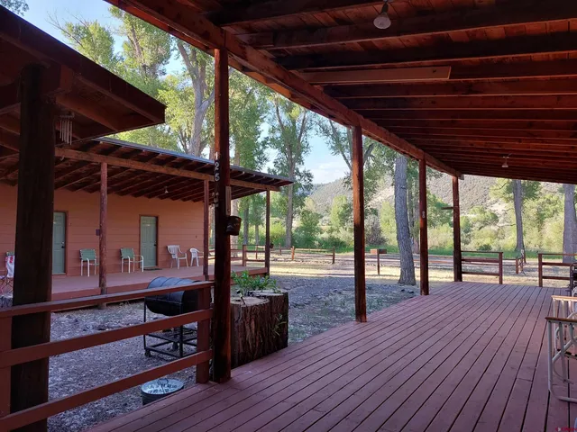 a view of a patio with table and chairs under wooden roof with a barbeque