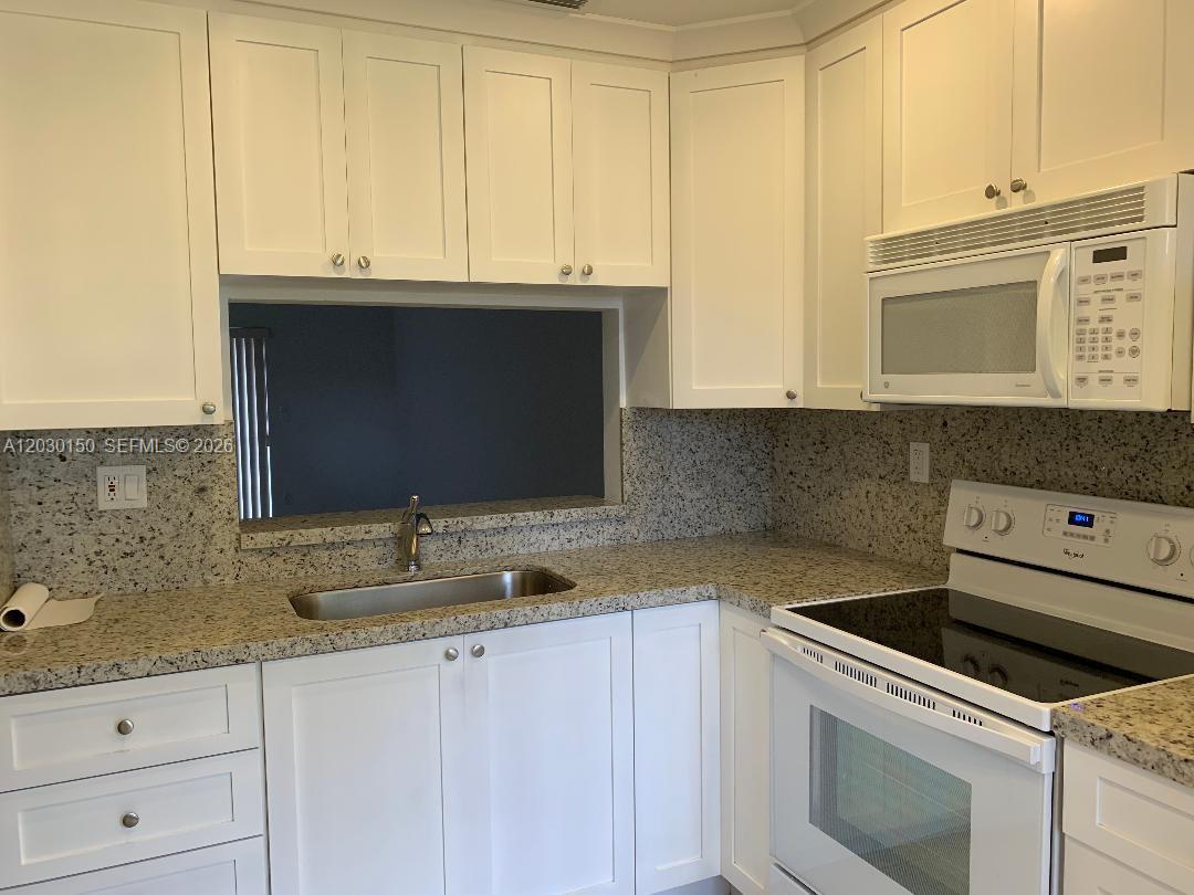 11206 Southwest 125th Place, Unit 11206 Miami, FL 33186 - Photo 3 of 15 a kitchen with granite countertop white cabinets sink and stainless steel appliances