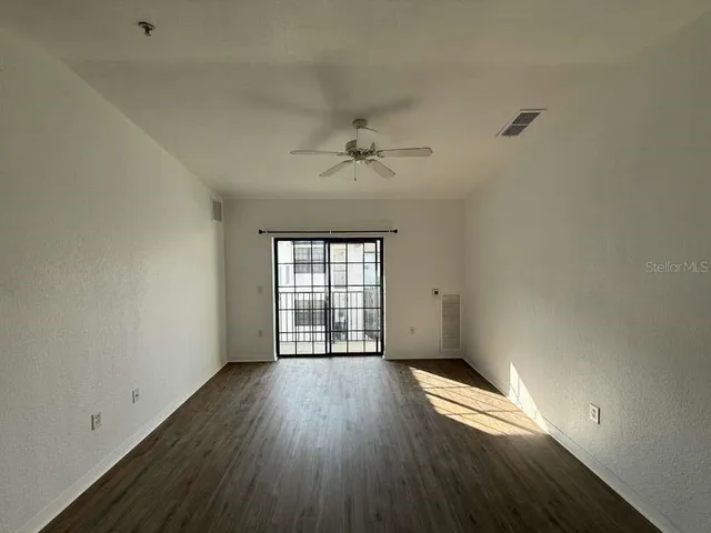 an empty room with wooden floor fan and windows