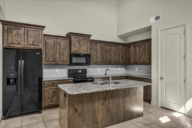 794 North Via Modelo Circle Washington, UT 84780 - Photo 8 of 21 Kitchen with black appliances, dark wood finish cabinetry, light tile patterned flooring, a center island with sink, and light stone countertops