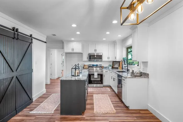 a kitchen with stainless steel appliances granite countertop a refrigerator a sink dishwasher a stove top oven a dining table and chairs with wooden floor