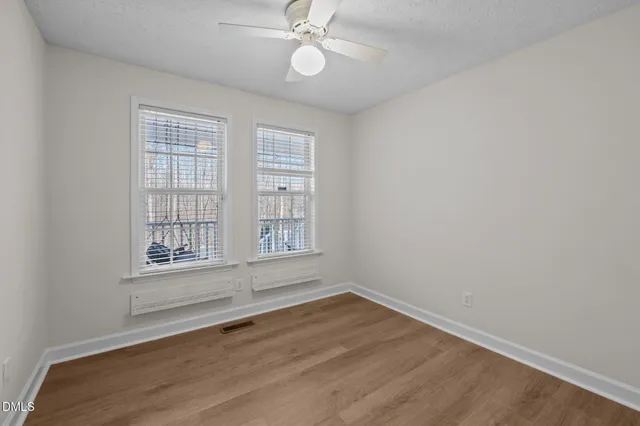 an empty room with wooden floor fan and windows