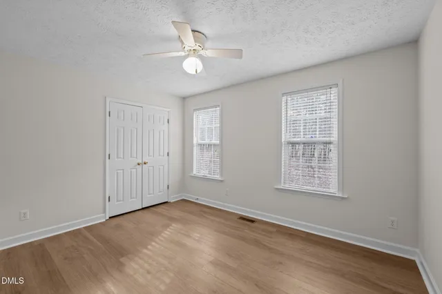 an empty room with wooden floor chandelier fan and windows