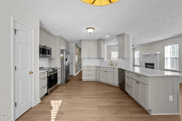 a large kitchen with stainless steel appliances kitchen island a stove a sink dishwasher a refrigerator and white cabinets with wooden floor