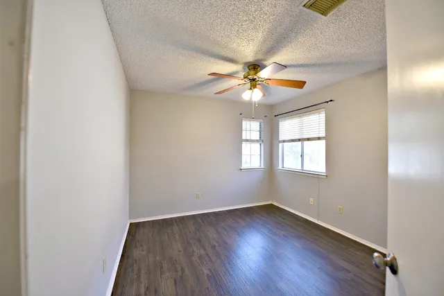 an empty room with wooden floor chandelier fan and windows