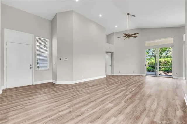 a view of an empty room with wooden floor kitchen view and a window