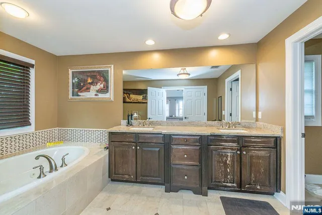 a bathroom with a tub double vanity sink and a large mirror