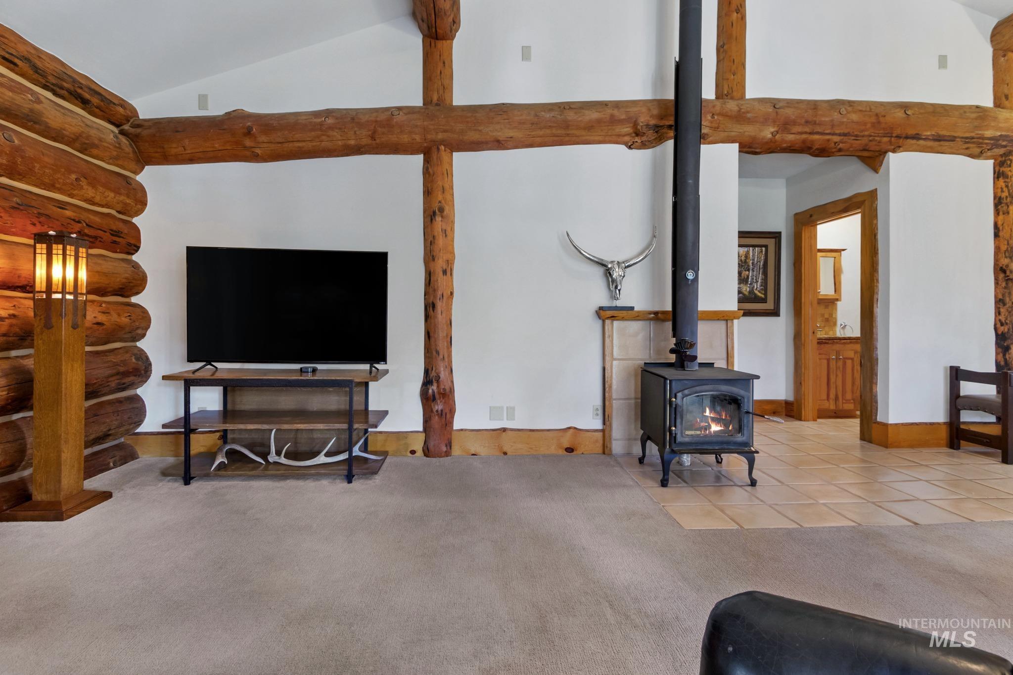 85 Pine Top Road Boise, ID 83716 - Photo 15 of 33 Living area featuring a cast iron wood-burning stove with a tiled hearth and a prominent log beam ceiling