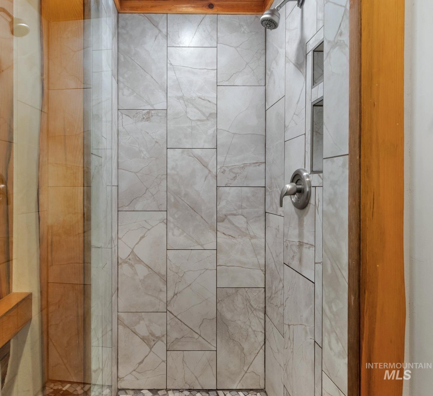 85 Pine Top Road Boise, ID 83716 - Photo 20 of 33 Walk-in shower featuring large format tile surround with a natural stone pattern, built-in shelving, glass enclosure, and pebble tile flooring