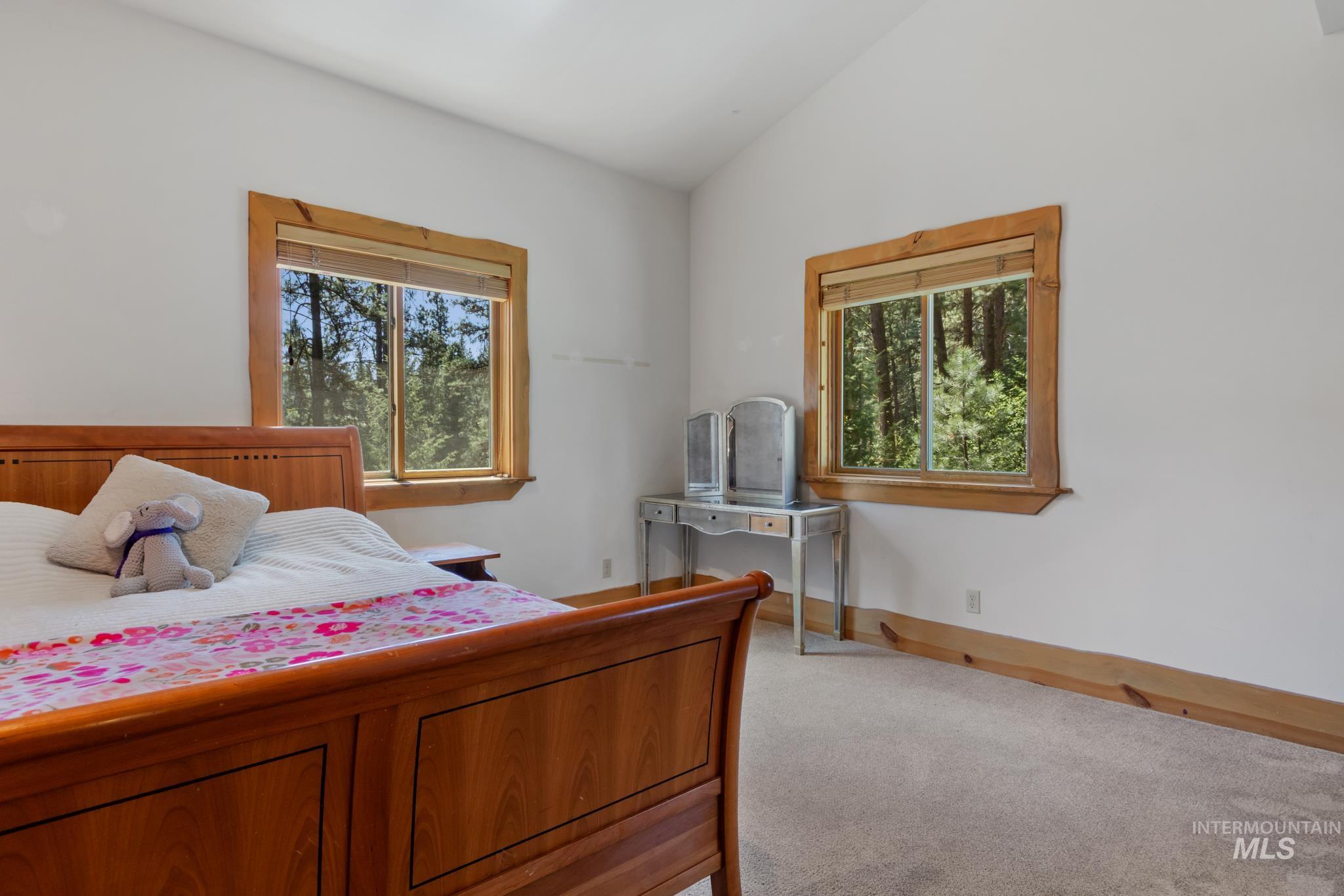 85 Pine Top Road Boise, ID 83716 - Photo 22 of 33 Bedroom featuring two large windows with natural wood trim, light neutral-toned carpeting, white walls, and a vaulted ceiling