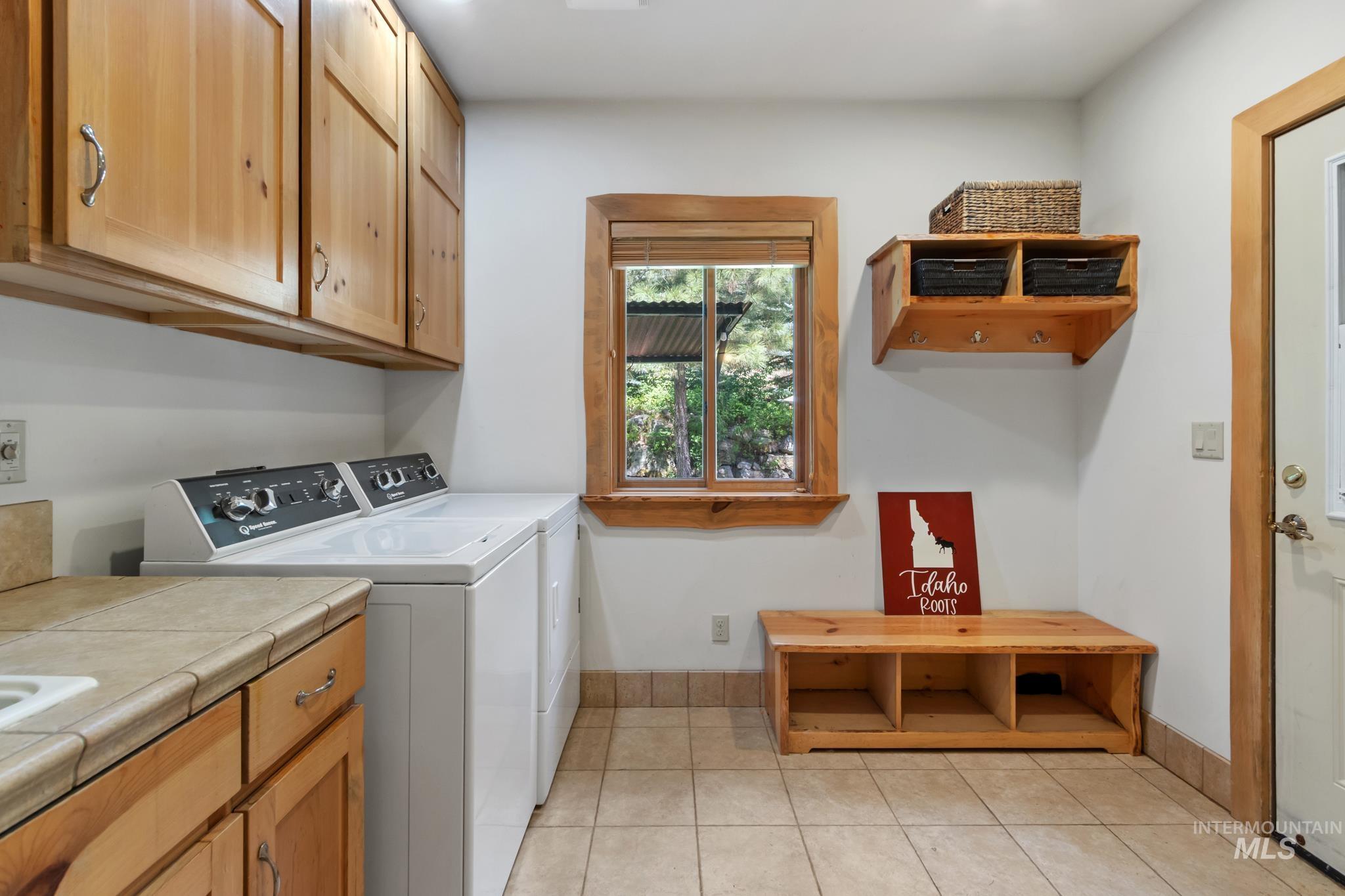85 Pine Top Road Boise, ID 83716 - Photo 23 of 33 Laundry area featuring wood cabinetry, a built-in sink with a tiled countertop, and a window with wood trim