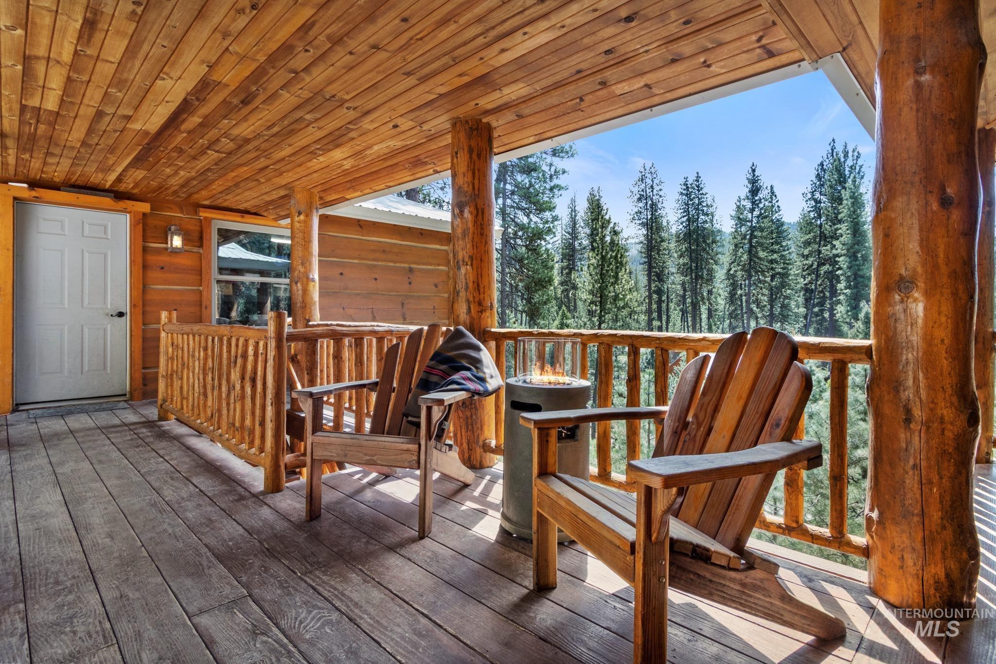 85 Pine Top Road Boise, ID 83716 - Photo 5 of 33 Covered wood-plank deck featuring a natural wood railing, log support columns, and a panoramic forest backdrop