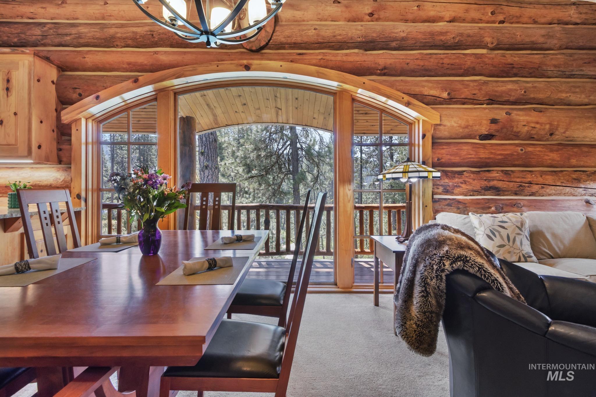 85 Pine Top Road Boise, ID 83716 - Photo 7 of 33 Dining area featuring a wood-finish dining table with seating for four, log-style wall construction, and a large arched window with exterior deck access