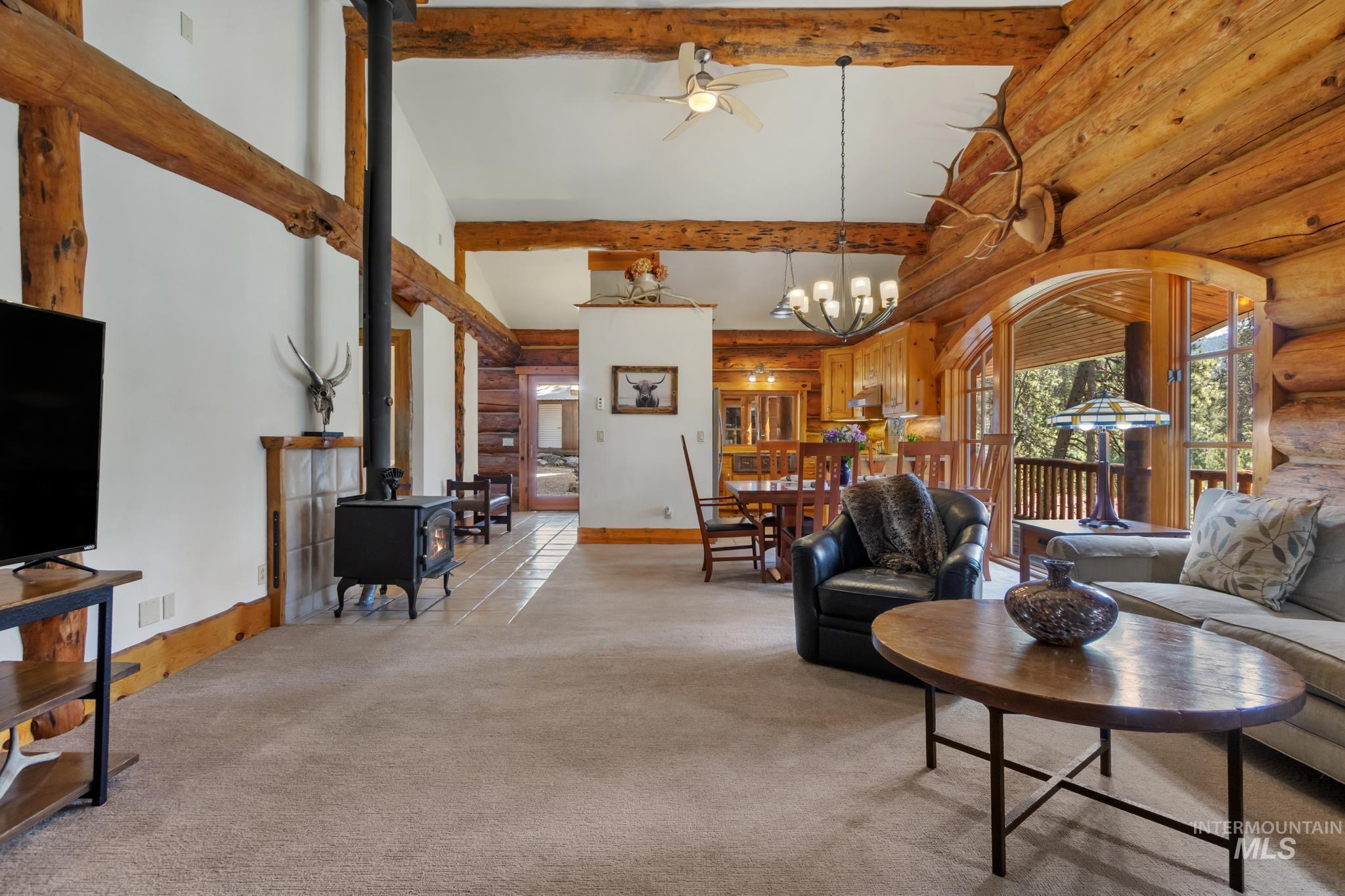 85 Pine Top Road Boise, ID 83716 - Photo 8 of 33 Spacious living area featuring exposed log beams, a black wood-burning stove with a tiled hearth, and carpet flooring