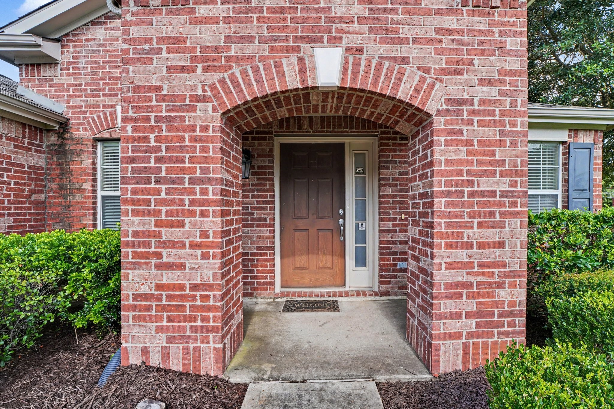 21427 Blooming Rock Lane Spring, TX 77379 - Photo 2 of 32 This photo shows a welcoming front entrance of a home with a red brick exterior and an arched doorway. The entryway is framed by tidy shrubs, creating a charming and inviting first impression.