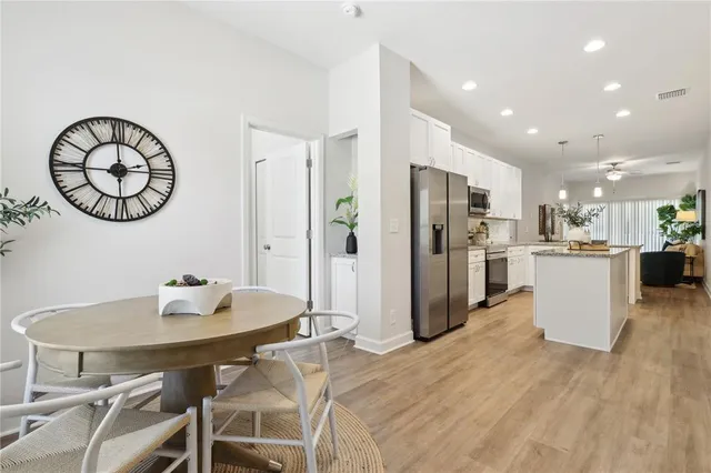 a kitchen with stainless steel appliances kitchen island granite countertop a dining table chairs and a refrigerator