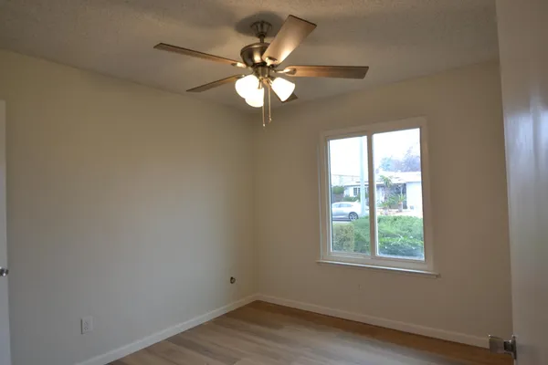 an empty room with wooden floor chandelier fan and windows