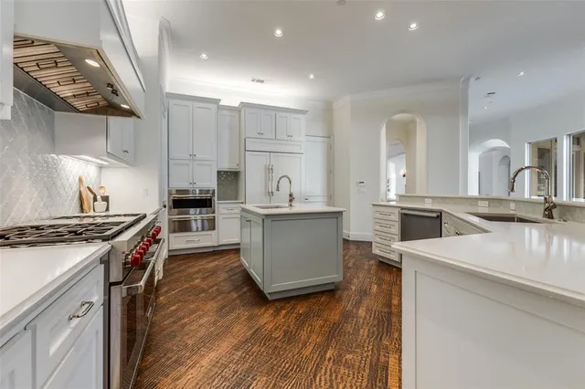 a kitchen with stainless steel appliances granite countertop a stove top oven a sink and white cabinets with wooden floor