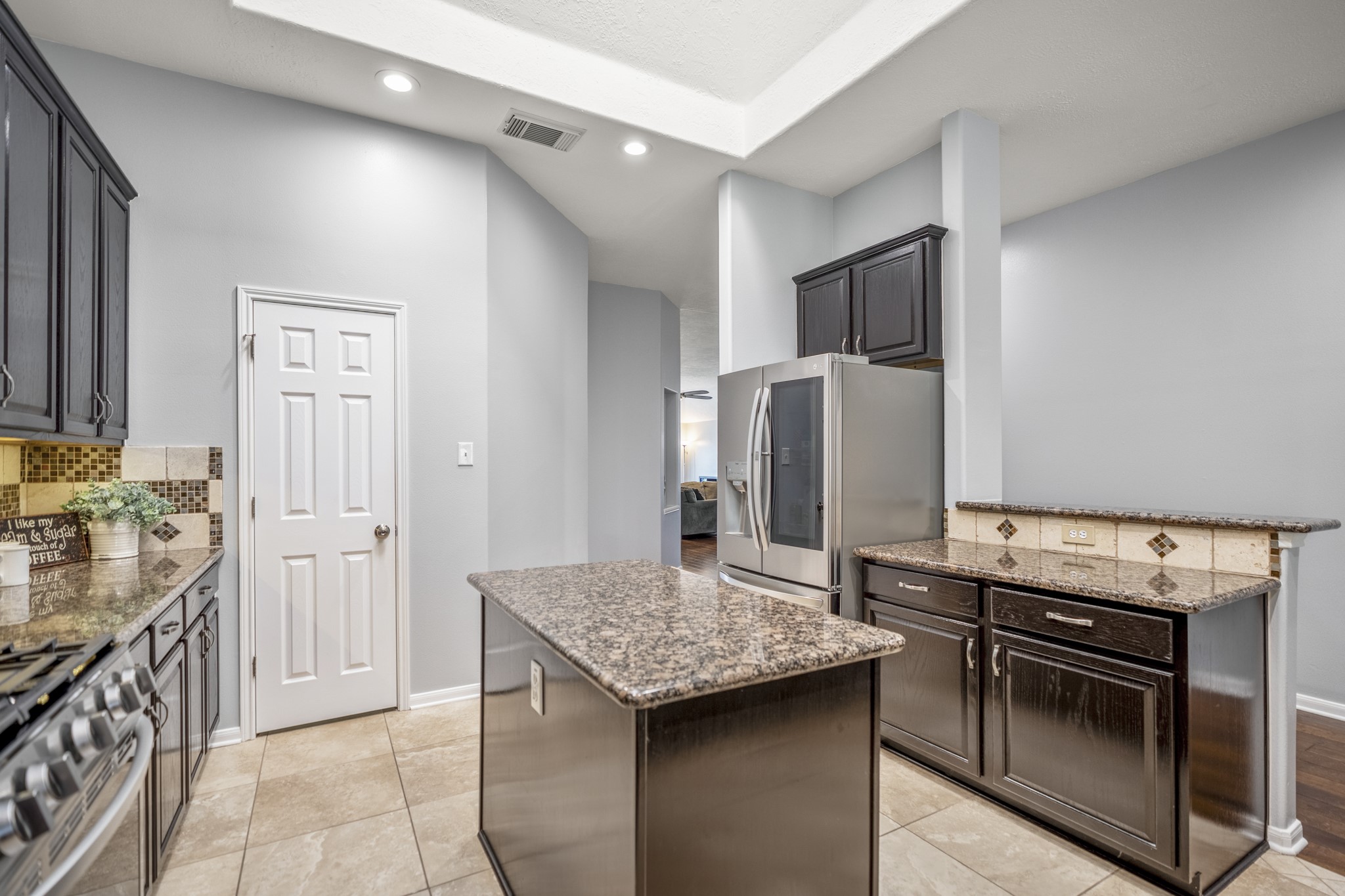 3411 Utah Beach Court Spring, TX 77388 - Photo 50 of 50 Just beyond the formal dining room, the kitchen starts to show why this floor plan lives so well, with an island, recessed lighting, generous counter space, and cabinetry wrapping the room. The pantry door sits ahead, the refrigerator and cooking area are positioned along the back wall, and the raised bar to the right helps connect the kitchen toward the breakfast room and family room beyond.