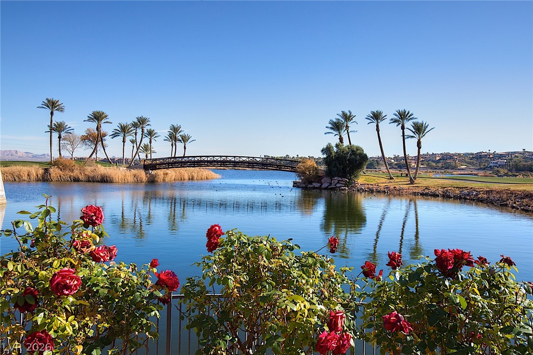 25 Falling Ridge Lane Henderson, NV 89011 - Photo 46 of 48 A tranquil lake with a picturesque bridge, surrounded by palm trees and vibrant flora, offers serene views.