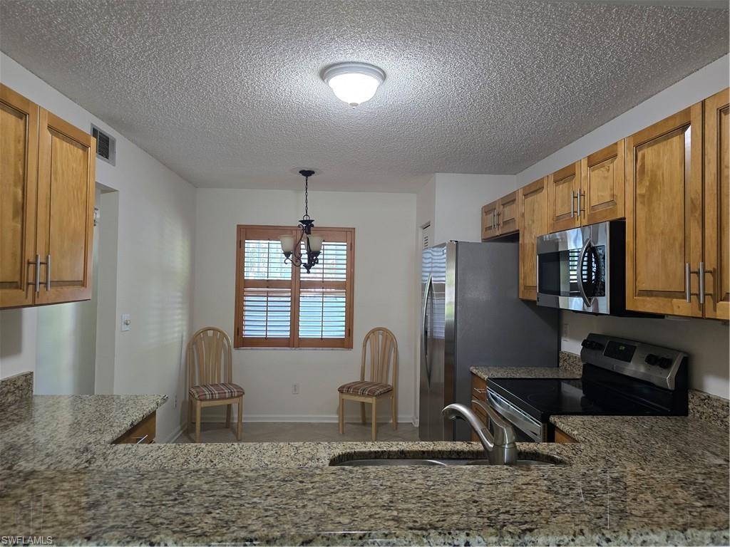 5737 Whitaker Road, Unit C104 Naples, FL 34112 - Photo 17 of 35 Granite countertops, wood cabinetry, stainless steel appliances, and a kitchen sink with a gooseneck faucet