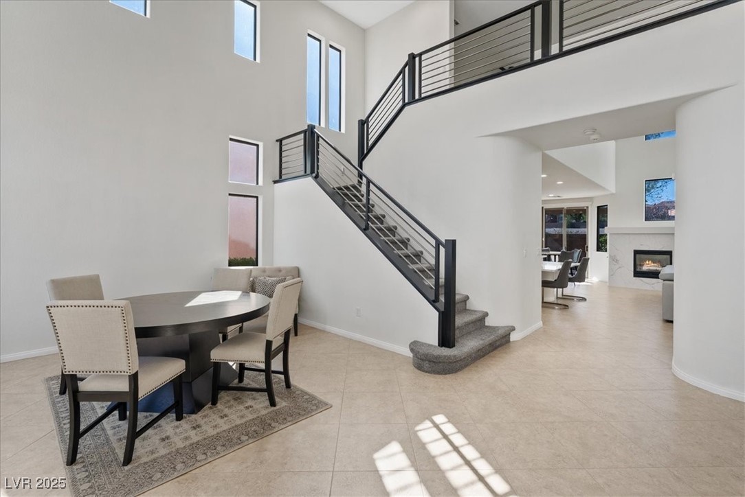 Dining space featuring a premium fireplace, stairs, a towering ceiling, healthy amount of natural light, and light tile patterned flooring