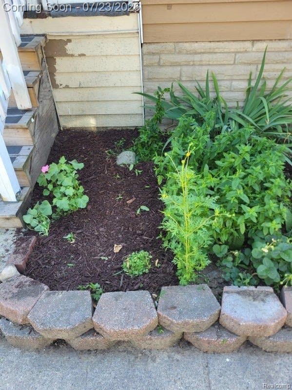 74 Pine Street River Rouge, MI 48218 - Photo 26 of 29 Landscaped garden bed featuring a segmented block retaining wall, dark wood mulch, and varied plantings