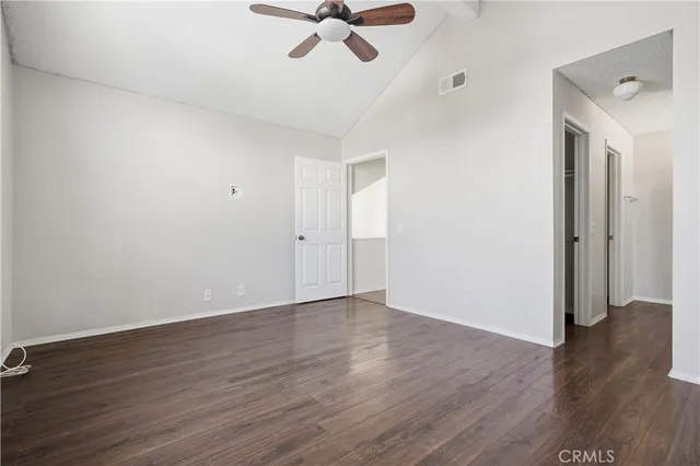 an empty room with wooden floor chandelier fan and windows
