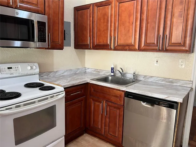 a kitchen with granite countertop a sink dishwasher stove and microwave with wooden cabinets