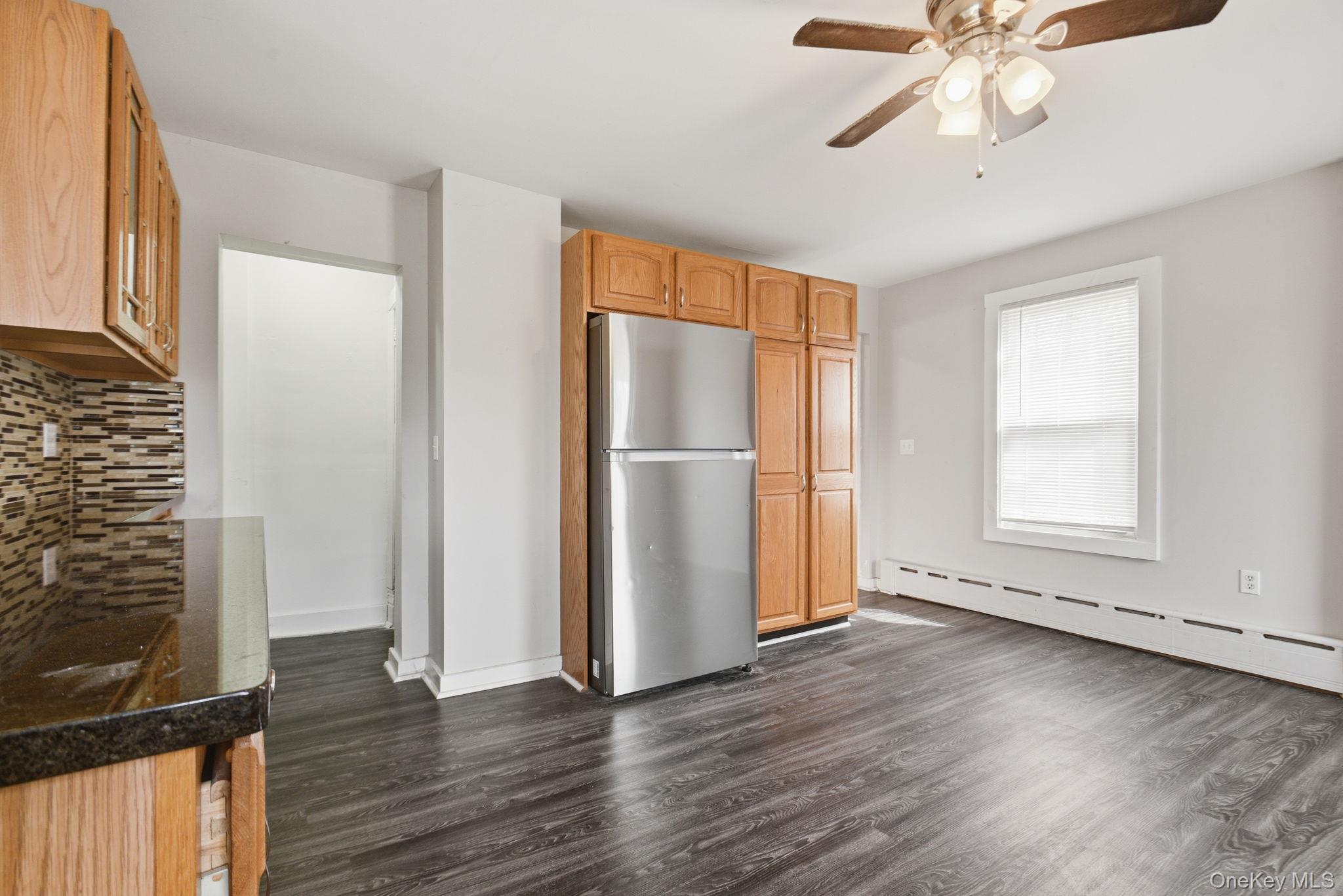 97 Maple Street Newburgh, NY 12550 - Photo 14 of 31 Kitchen featuring freestanding refrigerator, a baseboard heating unit, a ceiling fan, dark wood-style floors, and decorative backsplash