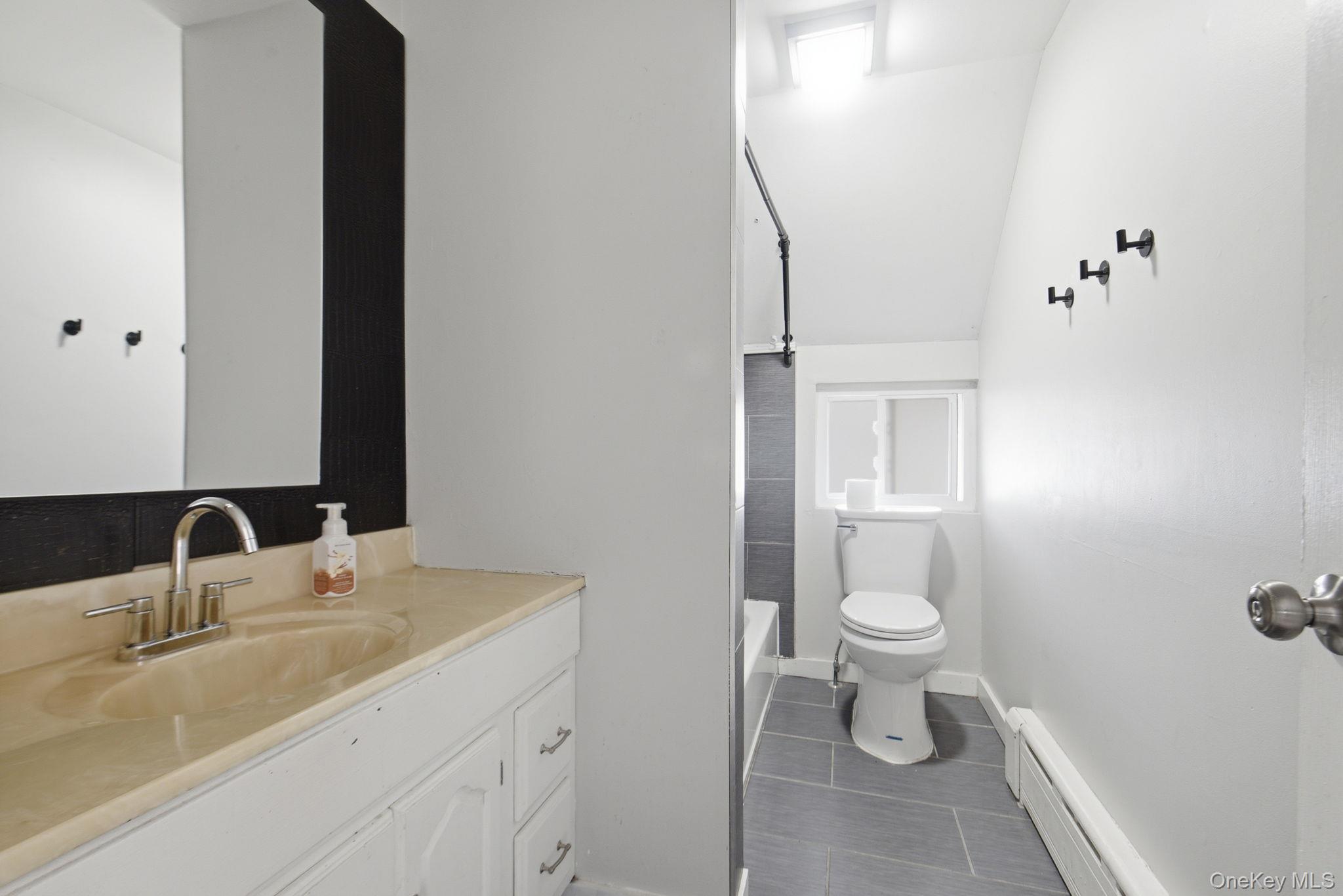 97 Maple Street Newburgh, NY 12550 - Photo 25 of 31 Full bathroom with vanity, baseboard heating, vaulted ceiling, and dark tile patterned flooring