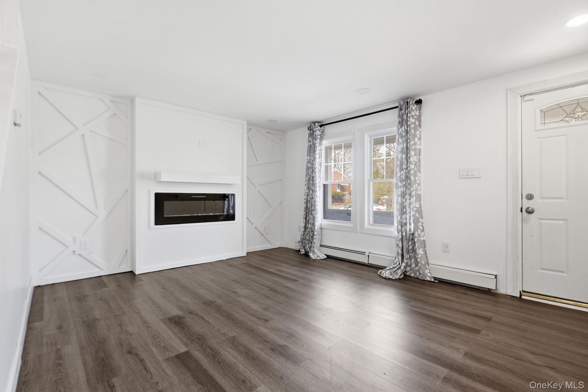 97 Maple Street Newburgh, NY 12550 - Photo 5 of 31 Unfurnished living room featuring dark wood-type flooring, a baseboard heating unit, and a glass covered fireplace