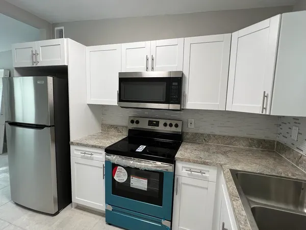 a view of a kitchen with a sink and dishwasher a refrigerator with white cabinets