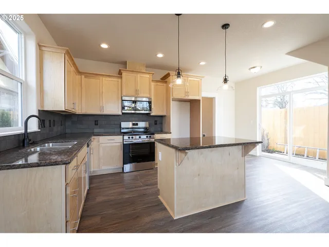 a kitchen with stainless steel appliances kitchen island granite countertop a stove a sink and a refrigerator with wooden floor